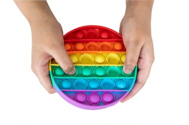 Hands of a young girl playing with a rainbow colored Popit. A bubble fidget sensory toy isolated on a white background.