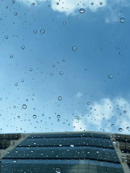 Selective focus on the rain droplets on the glass sunroof of a vehicle with blue sky in the background, after a downpour. Abstract concept.