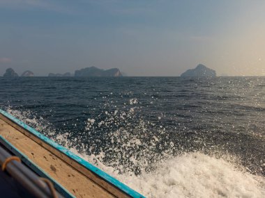 Tayland, Krabi 'de uzun kuyruklu bir teknenin kenarına çarpan dalgalar parlak beyaz bir sprey püskürtüyor ve okyanusun ham gücünü gösteriyor..