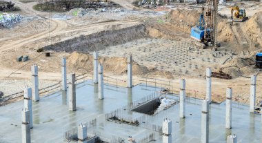 Construction site. The construction of a new house, a freshly poured concrete ceiling and frame pillars. In the background is a pile field in a pit with drilling rig and excavator