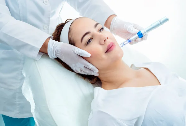 Faceless professional cosmetician in protective gloves applying liquid syringe with injection to client lying on medical equipment during beauty procedure in aesthetic cosmetology clinic