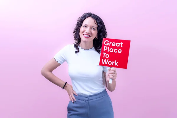 Cheerful adult female in casual outfit with curly hair demonstrating red sign with inscription great place to work