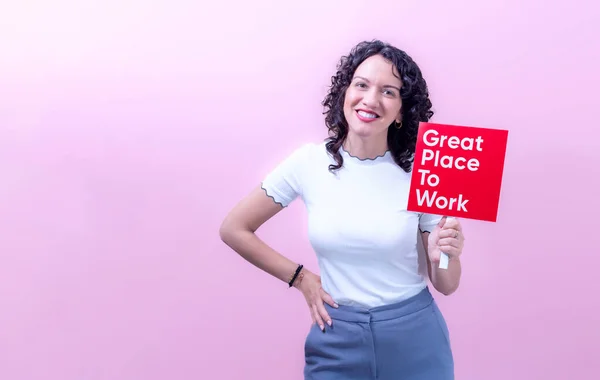 Cheerful adult female in casual outfit with curly hair demonstrating red sign with inscription great place to work copy space