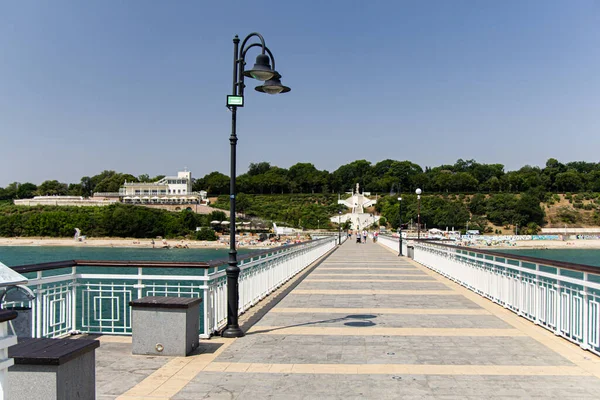 Önünde sokak lambası olan deniz kıyısında beyaz bir iskele. Denizde güneşli bir yaz günü. Yaz tatili