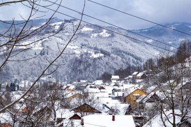 Kış boyunca karlı dağlarda, karla kaplı ağaçlarla çevrili birçok renkli çatı. Sakin bir kır manzarası..