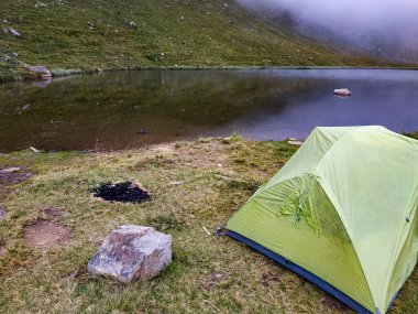 Göl kıyısında şöminesi olan yeşil bir çadır. Deniz kenarında kamp, açık hava macerası, seyahat ve doğa yaşam tarzı..