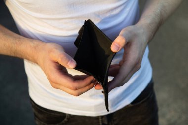 Erkek eli boş siyah bir cüzdan gösteriyor. Genç adam boş cüzdan ve artan faturalar yüzünden stresli. Ekonomik kriz kavramı ve yaşam stresinin maliyeti