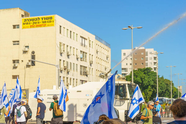 Haifa, Israel - July 11, 2023: Police water cannon vehicle, and people protest with flags and various signs. Part of day of disruption against controversial judicial overhaul, in Haifa, Israel