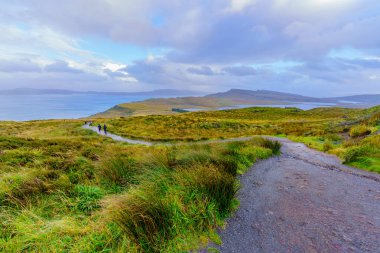 Portree, İngiltere - 30 Eylül 2022: Storr 'un Yaşlı Adamı yolu boyunca yürüyücülerle birlikte Skye Adası, İç Hebrides, İskoçya, İngiltere' de kayaların ve otların gün batımı manzarası