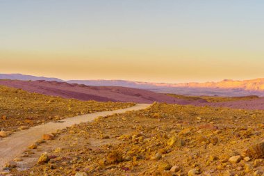 Güney İsrail 'deki Negev Çölü' nde, bir patika ve Makhtesh (krater) Ramon 'un manzarasının günbatımı manzarası. Büyük bir erozyon sirkinin jeolojik bir alanı.