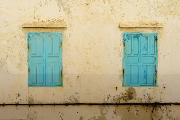 Mavi pencereler ve panjurlar beyaz boyalı eski bir evin duvarında. Essaouira (Mogador), Fas