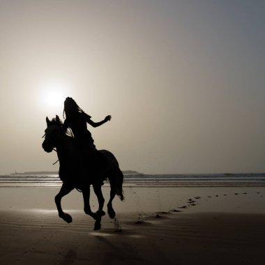 Bir atın silueti ve binicisi Essaouira sahilinde (Mogador), Fas