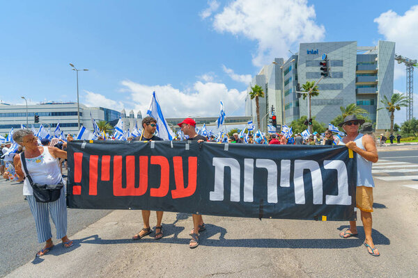 Haifa, Israel - July 07, 2024: People protest with flags, various signs, blocking a major junction. Part of day of disruption against the government and support of hostages families, Haifa, Israel