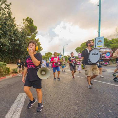 Hayfa, İsrail - 24 Ağustos 2024: İnsanlar, hükümete karşı çeşitli işaret ve bayraklarla yeni seçimler çağrısında bulunan bir protesto yürüyüşüne (pembe grup) katılıyor. Hayfa, İsrail