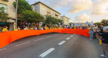 Hayfa, İsrail - 29 Ağustos 2024: Rehine kurdelesi taşıyan insanlar, rehine anlaşması çağrısında bulunan bir protesto gösterisinin parçası olarak sokakta yürüyor. Hayfa, İsrail