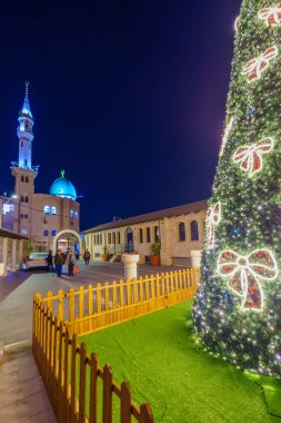 Shefa-Amr, İsrail - 19 Aralık 2024: St. Peter ve St. Paul Kilisesi 'nin bahçesi, bir Noel ağacı ve arka planda Eski Cami. Shefa-Amr (Shfaram), İsrail
