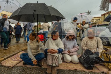 Hayfa, İsrail - 27 Aralık 2024: Şiddetli yağmur altında beyaz koltukta oturan insanlar, 101 vardiya protestosunun bir parçası olarak Hayfa, İsrail 'de rehine anlaşması çağrısında bulundular
