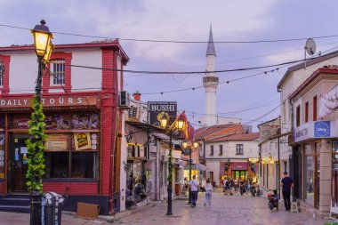Üsküp, Kuzey Makedonya - 06 Ekim 2023: Eski Pazar semtinde dükkanlar, yerel halk ve ziyaretçilerle gün batımı sokak sahnesi. Üsküp, Kuzey Makedonya