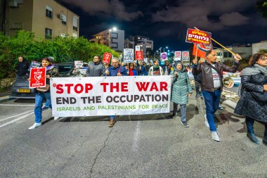 Hayfa, İsrail - 08 Şubat 2025: İnsanlar çeşitli işaret ve bayraklarla bir protesto yürüyüşüne katılıyor, savaşı sona erdirme ve rehine anlaşmasının tamamlanması çağrısında bulunuyorlar. Hayfa, İsrail