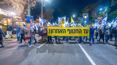 Hayfa, İsrail - 15 Şubat 2025: Çeşitli tabela ve bayraklara sahip insanlar savaşın sona ermesi, rehine anlaşmasının tamamlanması ve yeni seçimler için düzenlenen protesto mitingine katıldılar. Hayfa, İsrail