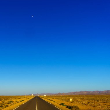 Arka planda Atlas Dağları olan bir çöl yolu manzarası. Merkez Fas