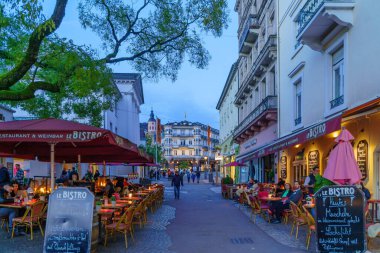 Baden-Baden, Almanya - 13 Ekim 2024: Baden-Baden, Baden-Wurttemberg, Almanya 'da çeşitli binalar, yerliler ve ziyaretçilerle birlikte günbatımı sokak manzarası