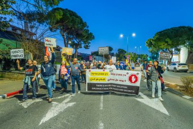 Hayfa, İsrail - 15 Mart 2025: İnsanlar çeşitli işaret ve bayraklarla bir protesto yürüyüşüne katılıyor, savaşın sona ermesi ve rehine anlaşmasının tamamlanması çağrısında bulunuyorlar. Hayfa, İsrail