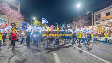Hayfa, İsrail - 15 Mart 2025: Çeşitli tabelaları ve bayrakları olan insanlar, savaşın sona ermesi, rehine anlaşmasının tamamlanması ve yeni seçimlerin başlatılması için düzenlenen protesto mitingine katıldılar. Hayfa, İsrail