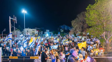 Hayfa, İsrail - 15 Mart 2025: Çeşitli tabela ve bayraklara sahip bir grup insan, savaşın sona ermesi, rehine anlaşmasının tamamlanması ve yeni seçimler için düzenlenen protesto mitingine katıldı. Hayfa, İsrail