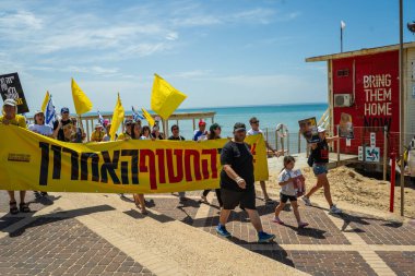 Hayfa, İsrail - 28 Mart 2025: İnsanlar, Hamas aileleri tarafından kaçırılan rehinelere destek olmak amacıyla sahil boyunca pankartlar, pankartlar ve bayraklarla yürüyüş yaparak anlaşma çağrısında bulundular. Hayfa, İsrail