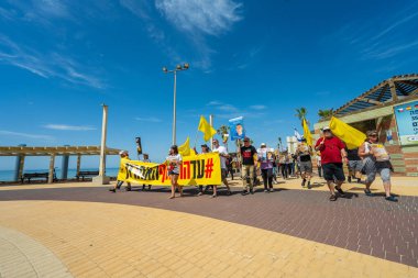 Hayfa, İsrail - 28 Mart 2025: İnsanlar, Hamas aileleri tarafından kaçırılan rehinelere destek olmak amacıyla sahil boyunca pankartlar, pankartlar ve bayraklarla yürüyüş yaparak anlaşma çağrısında bulundular. Hayfa, İsrail