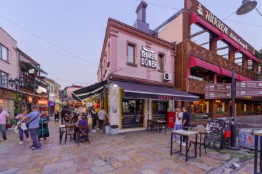 Üsküp, Kuzey Makedonya - 05 Ekim 2023: Eski Pazar semtinde dükkanlar, yerel halk ve ziyaretçilerle gün batımı sokak sahnesi. Üsküp, Kuzey Makedonya