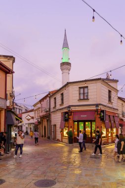 Üsküp, Kuzey Makedonya - 06 Ekim 2023: Eski Pazar semtinde dükkanlar, yerel halk ve ziyaretçilerle gün batımı sokak sahnesi. Üsküp, Kuzey Makedonya