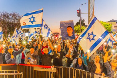 Hayfa, İsrail - 19 Nisan 2025: Çeşitli tabela ve bayraklara sahip bir grup insan, savaşın sona ermesi, rehine anlaşmasının tamamlanması ve yeni seçimler için düzenlenen protesto mitingine katıldı. Hayfa, İsrail