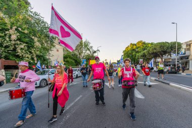 Hayfa, İsrail - 19 Nisan 2025: İnsanlar savaşın sona ermesi, rehine anlaşmasının tamamlanması ve yeni seçimler çağrısında bulunan bir protesto yürüyüşüne (Pembe Cephe Grubu) katılıyor. Hayfa, İsrail