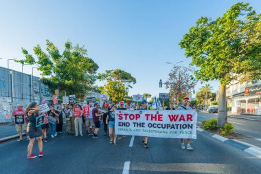 Hayfa, İsrail - 28 Haziran 2025: İnsanlar çeşitli işaret ve bayraklarla bir protesto yürüyüşüne katılıyor, savaşın sona ermesi ve rehine anlaşmasının tamamlanması çağrısında bulunuyorlar. Hayfa, İsrail