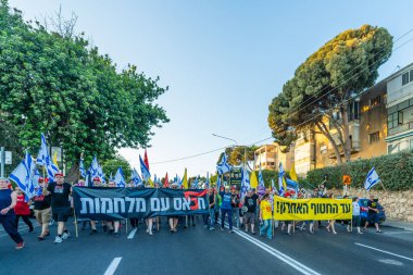 Hayfa, İsrail - 28 Haziran 2025: Çeşitli tabelaları ve bayrakları olan insanlar, savaşın sona ermesi, rehine anlaşmasının tamamlanması ve yeni seçimlerin başlatılması için düzenlenen protesto mitingine katıldılar. Hayfa, İsrail