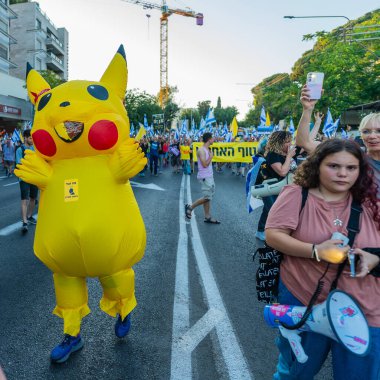 Hayfa, İsrail - 28 Haziran 2025: İnsanlar (Pikachu kostümlü adamla birlikte) savaşın sona ermesi, rehine anlaşmasının tamamlanması ve yeni seçimler çağrısında bulunan bir protesto yürüyüşüne katılıyor. Hayfa, İsrail