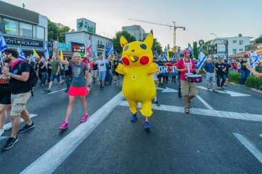 Hayfa, İsrail - 28 Haziran 2025: İnsanlar (Pikachu kostümlü adamla birlikte) savaşın sona ermesi, rehine anlaşmasının tamamlanması ve yeni seçimler çağrısında bulunan bir protesto yürüyüşüne katılıyor. Hayfa, İsrail