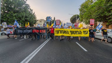 Hayfa, İsrail - 12 Temmuz 2025: Çeşitli tabelaları ve bayrakları olan insanlar, savaşın sona ermesi, rehine anlaşmasının tamamlanması ve yeni seçimlerin başlatılması için düzenlenen protesto mitingine katıldılar. Hayfa, İsrail
