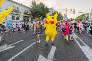 Hayfa, İsrail - 12 Temmuz 2025: İnsanlar (Pikachu kostümlü adamla birlikte) savaşın sona ermesi, rehine anlaşmasının tamamlanması ve yeni seçimler çağrısında bulunan bir protesto yürüyüşüne katılıyor. Hayfa, İsrail