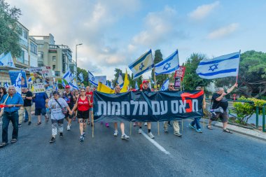Hayfa, İsrail - 19 Temmuz 2025: Çeşitli tabelaları ve bayrakları olan insanlar, savaşın sona ermesi, rehine anlaşmasının tamamlanması ve yeni seçimlerin başlatılması için düzenlenen protesto mitingine katıldılar. Hayfa, İsrail