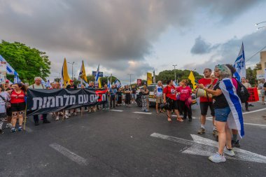 Hayfa, İsrail - 19 Temmuz 2025: Çeşitli tabelaları ve bayrakları olan insanlar, savaşın sona ermesi, rehine anlaşmasının tamamlanması ve yeni seçimlerin başlatılması için düzenlenen protesto mitingine katıldılar. Hayfa, İsrail