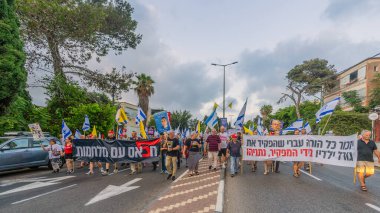 Hayfa, İsrail - 19 Temmuz 2025: Çeşitli tabelaları ve bayrakları olan insanlar, savaşın sona ermesi, rehine anlaşmasının tamamlanması ve yeni seçimlerin başlatılması için düzenlenen protesto mitingine katıldılar. Hayfa, İsrail