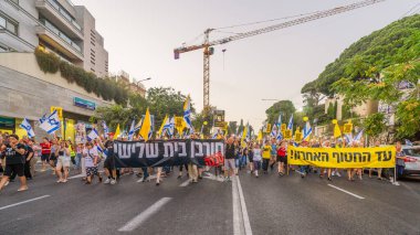 Hayfa, İsrail - 09 Ağustos 2025: Çeşitli tabelaları ve bayrakları olan insanlar, savaşın sona ermesi, rehine anlaşmasının tamamlanması ve yeni seçimlerin başlatılması için düzenlenen protesto mitingine katıldılar. Hayfa, İsrail