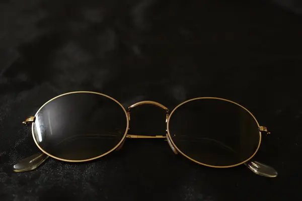 Beyaz arka planda altın mercekli siyah güneş gözlüğü.