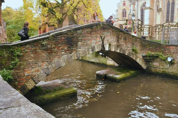 stock image 30-10-2014 Bruges, Belgium - Tourists cross a picturesque stone and brick bridge over a Bruges canal