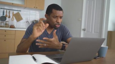 Gülümseyen Afro-Amerikan iş adamı evde dizüstü bilgisayar kullanıyor. Siyahi adam bilgisayardan müşteriyle görüntülü konuşma yapıyor. İşi uzaktan çözme modern teknoloji ve video çağrı etkinliği kavramını kullan