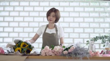 Beautiful florist Entrepreneur Asian woman chooses flowers for future bouquet in flower shop. Floral design studio, making decorations and arrangements. Flowers delivery, creating order. SME Concept.