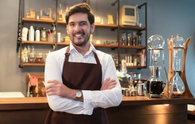 Yakışıklı beyaz garson küçük işletme sahibi kahverengi önlüklü barista restoranda barın tezgahında kollarını kavuşturmuş kameraya bakıyor. Mutlu Adam KOBİ kavramı ile çalışıyor.